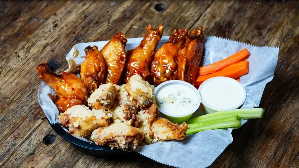 Rustic basket of sauced and seasoned chicken wings, carrots, celery, dips.
