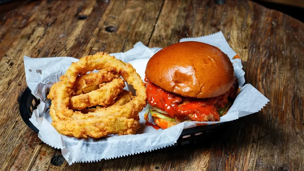Burger with red sauce and crispy golden onion rings in a basket.