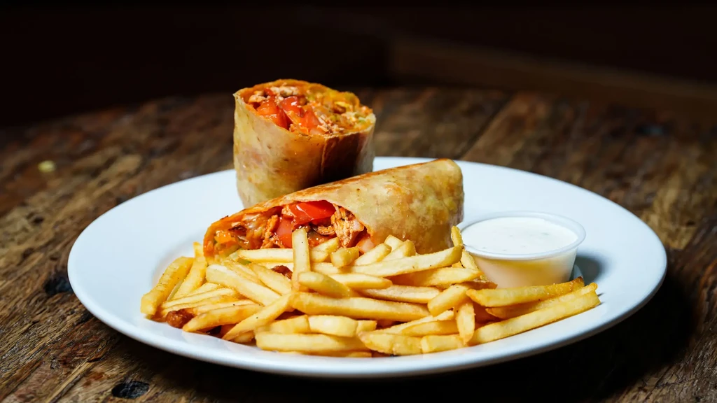 Chicken wrap halves, golden fries, and dipping sauce on wood.