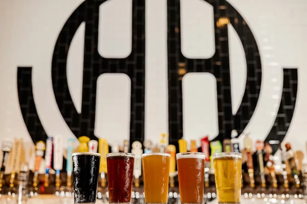 Five different cold beers on a bar, with taps and a logo.