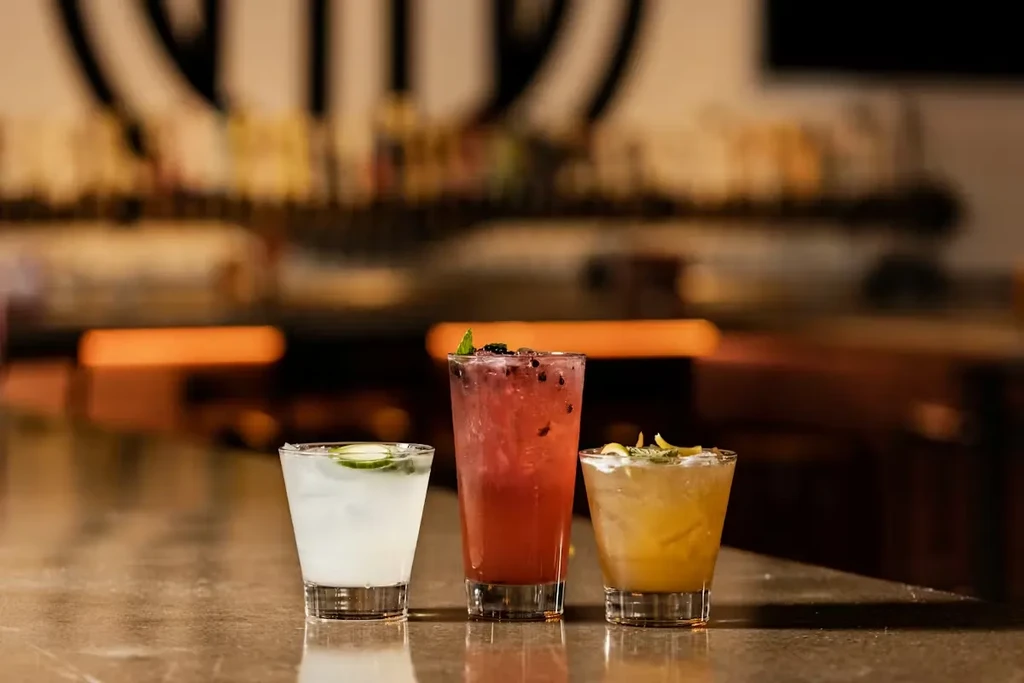 White, pink, and orange cocktails with garnishes on a stone bar.