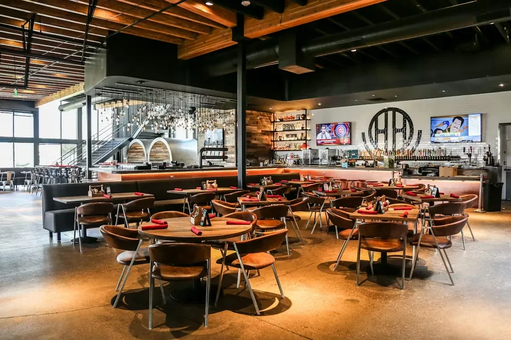 Modern industrial restaurant interior with tables, a bar, and exposed beams.