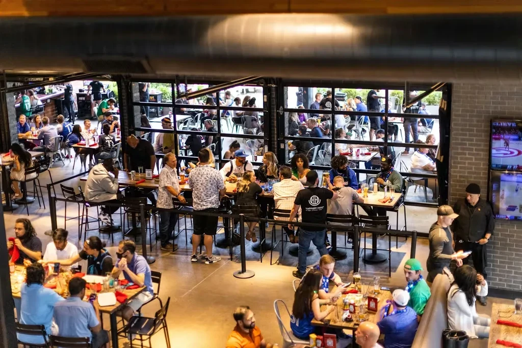 Lively restaurant and patio with people eating, drinking, and watching sports.