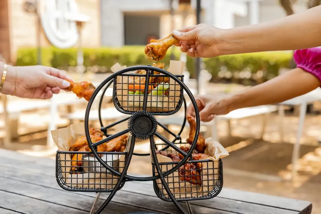 Multiple hands take chicken wings from a Ferris wheel serving stand.