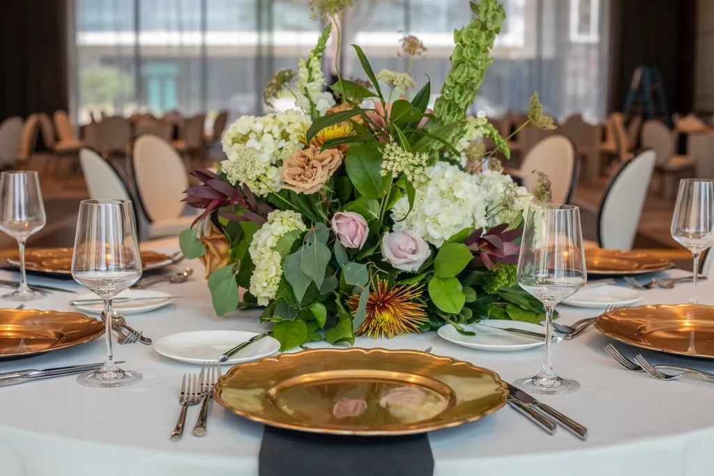 Round table with elaborate floral centerpiece and gold place settings.