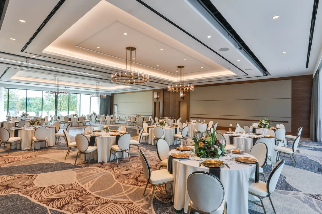 Spacious, empty banquet hall with set tables, modern chandeliers, green view.