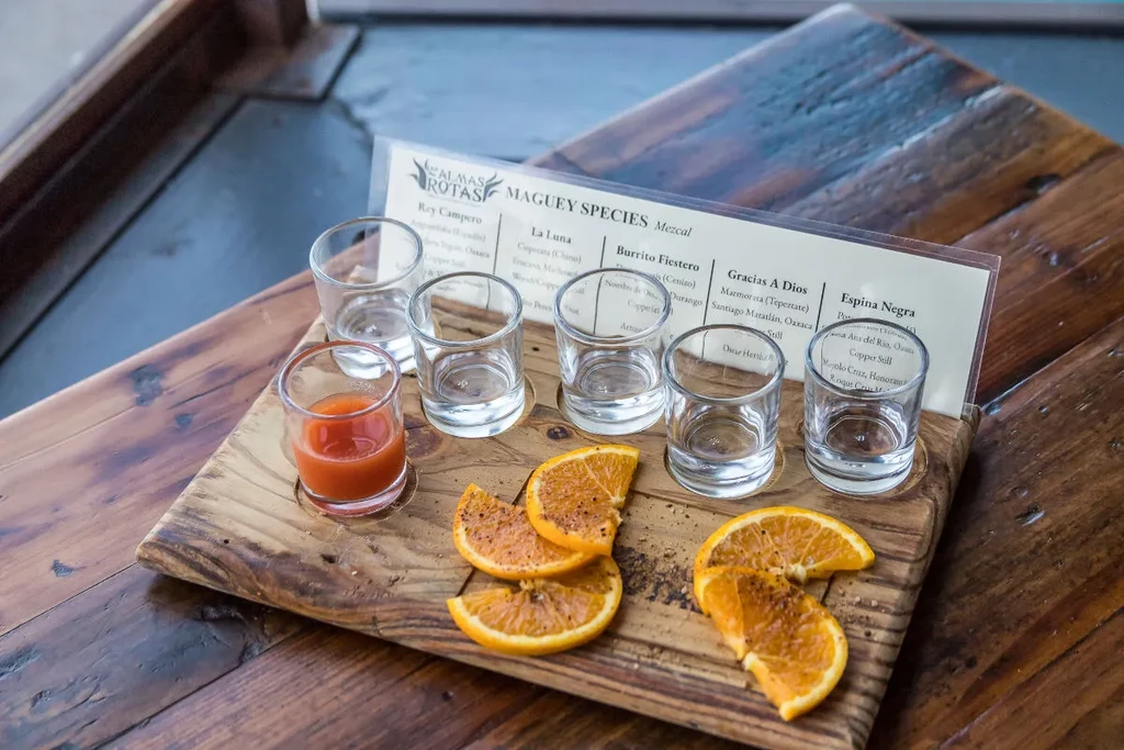 Mezcal tasting flight with glasses, seasoned oranges, and Maguey Species card.