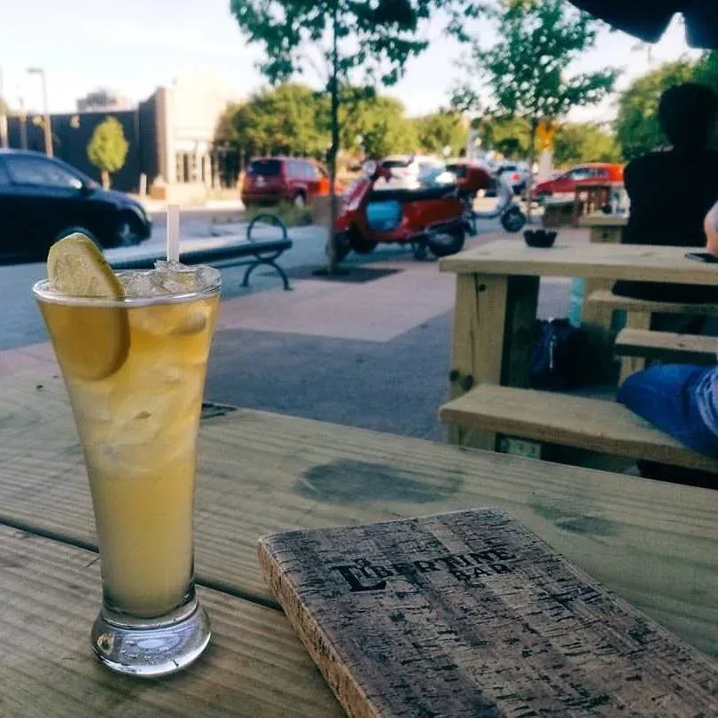 Iced yellow drink with lime and menu on an outdoor table.