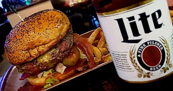 Dimly lit burger, fries, and Miller Lite beer can on a plate.