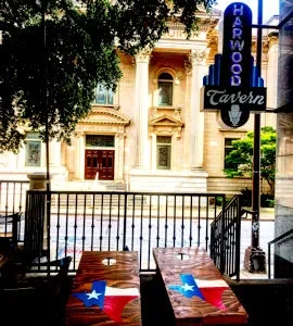 Texas flag cornhole boards, Harwood Tavern sign, and a grand building.