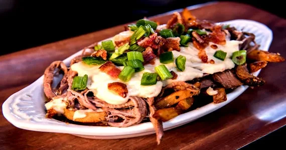 Boat dish loaded with fries, shredded meat, creamy sauce, green onions.