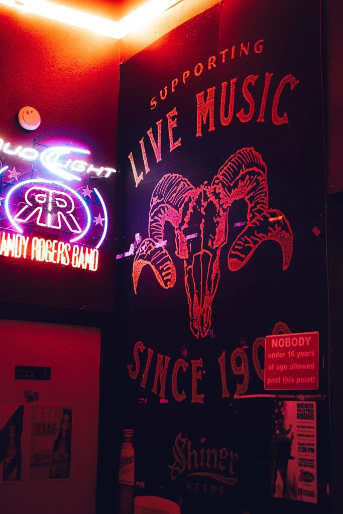 Neon-lit bar corner with signs for music, beer, and rodeo.
