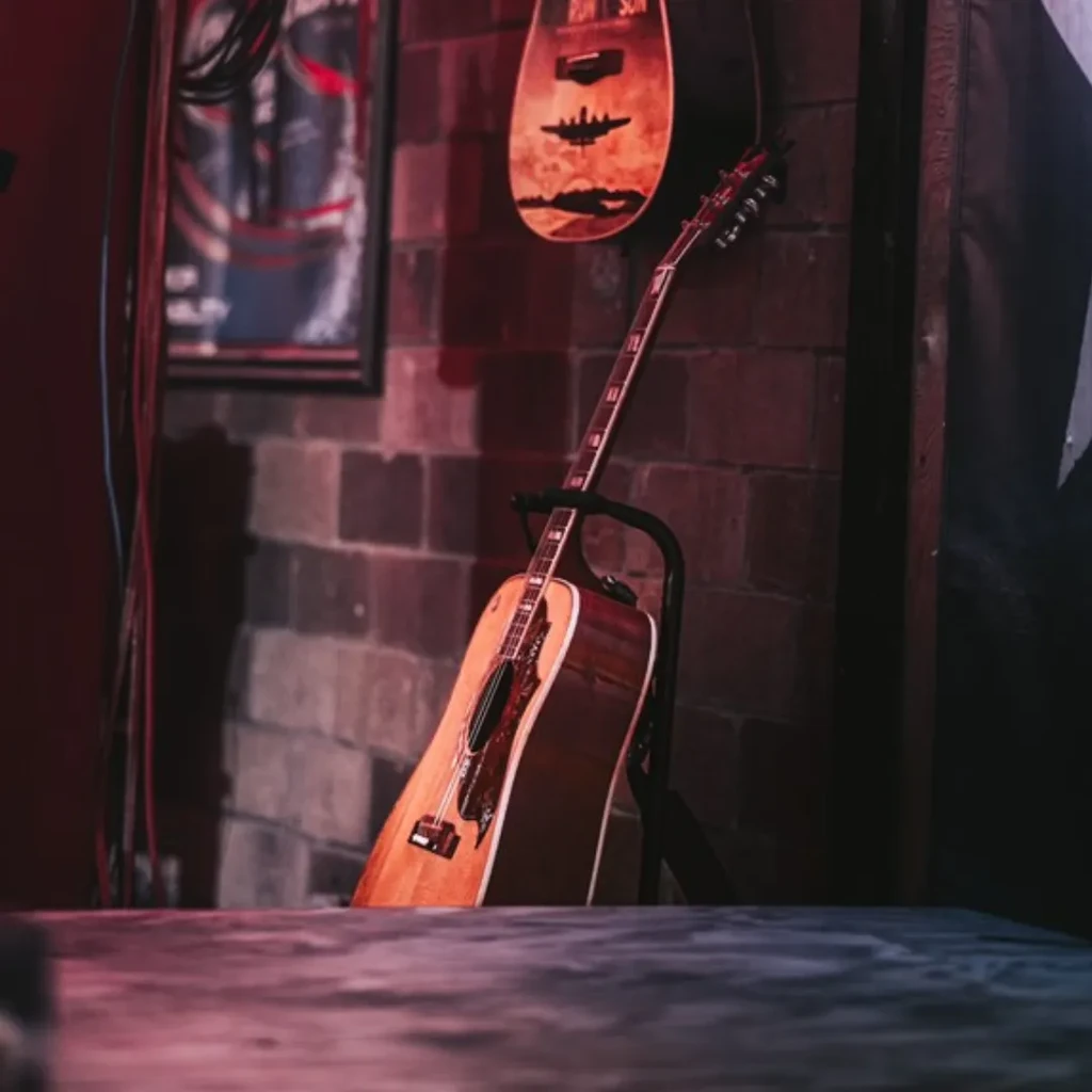 Acoustic guitar on stand against brick wall, with decorative guitar above.