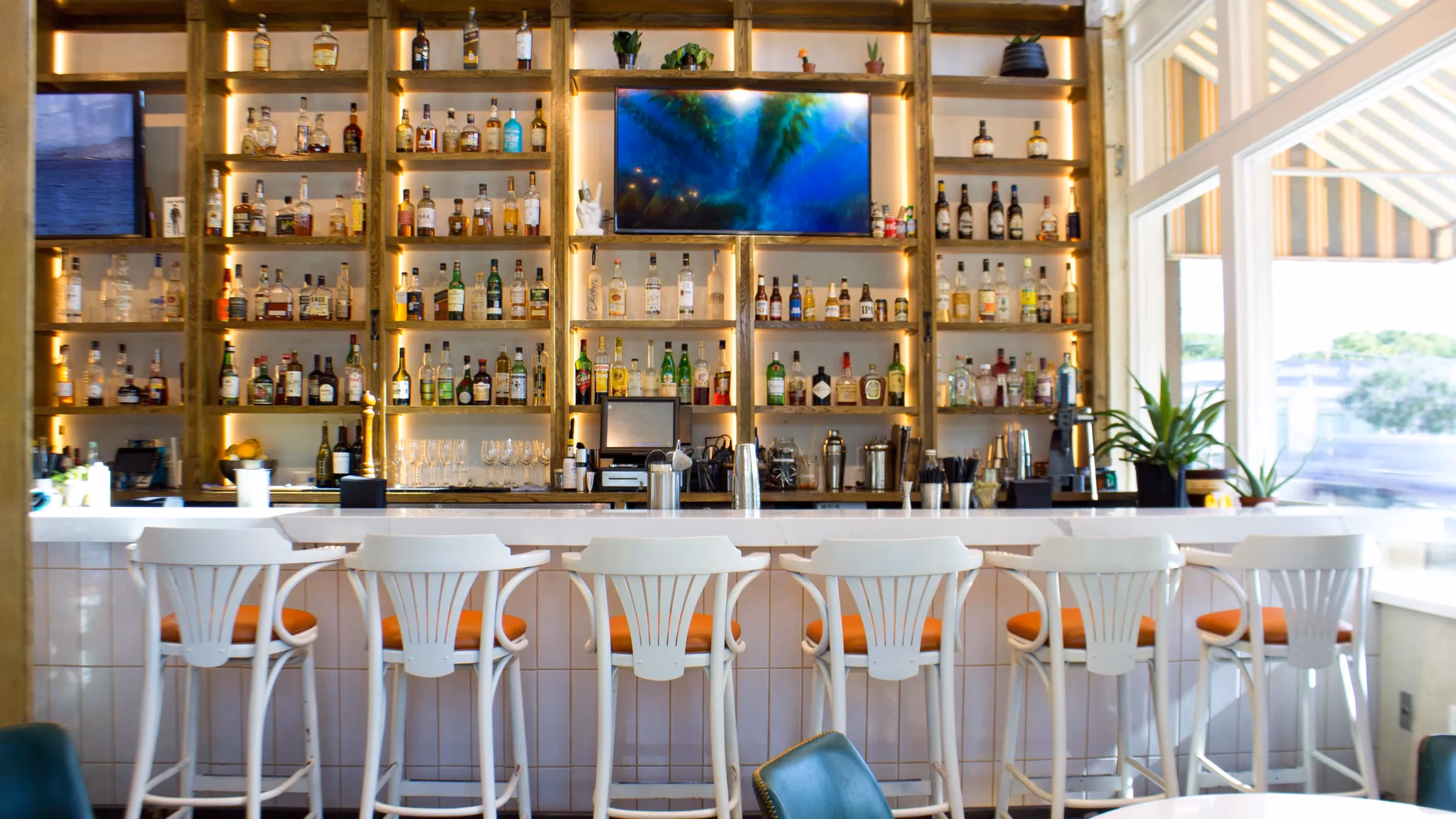A well-lit bar with shelves of liquor bottles and white bar stools.