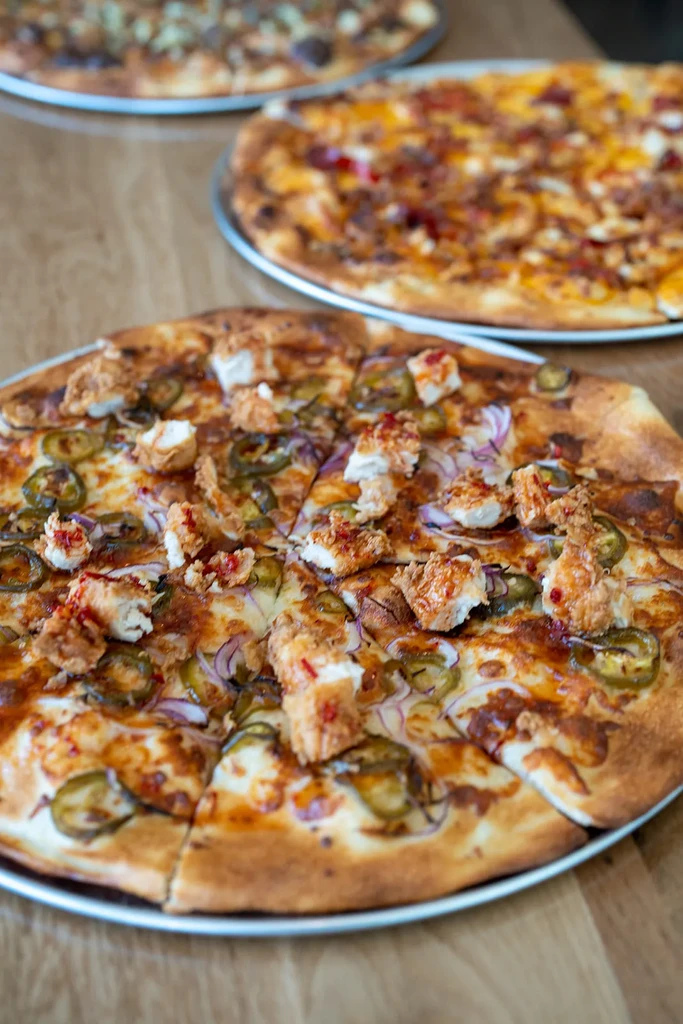 Crispy chicken, onion, jalapeño pizza with sauce on a light brown wooden table.