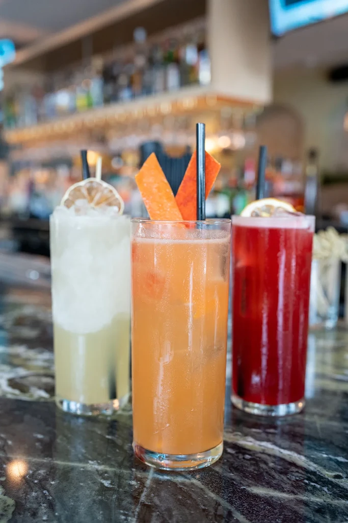Three vibrant, garnished cocktails on a reflective marble bar.