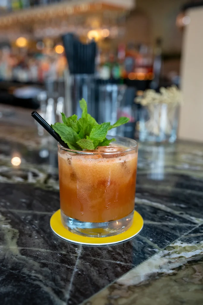 Foamy orange-brown drink with mint and straw on a bar counter.