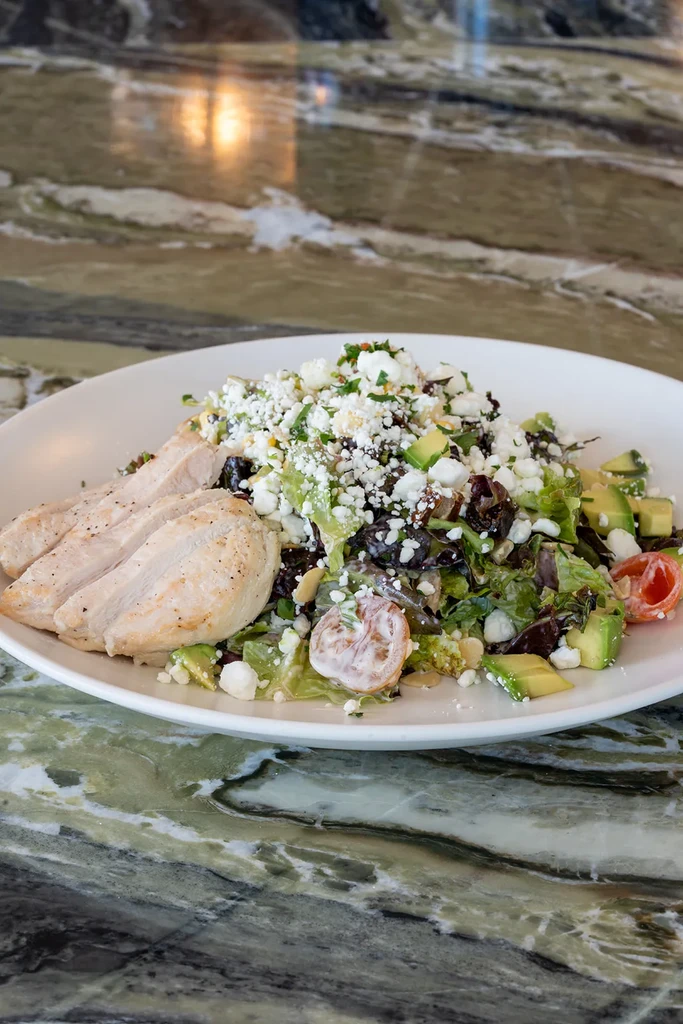 Sliced grilled chicken salad with greens, avocado, tomatoes, feta.