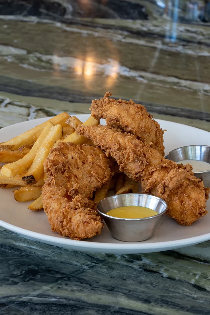 Crispy chicken tenders, salted fries, and two dipping sauces on a plate.