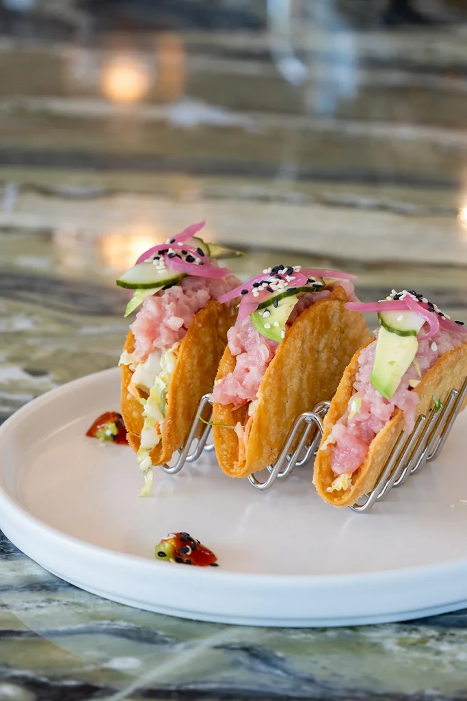 Three crispy mini tacos with raw fish, avocado, and pickled onions.