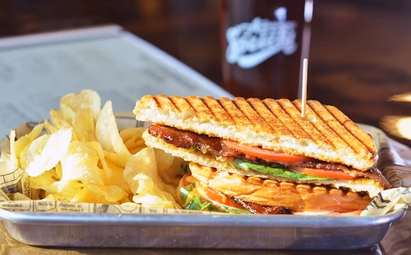 Grilled sandwich with bacon, tomato, lettuce, and potato chips.