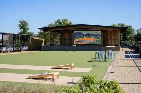 Outdoor entertainment zone with large screen baseball, cornhole, and seating.
