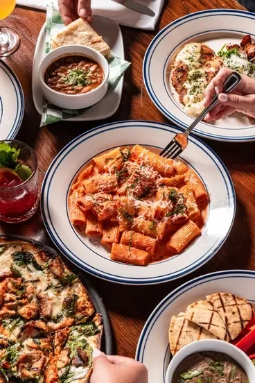 Group eating pasta, pizza, chicken, and beans at a restaurant table.