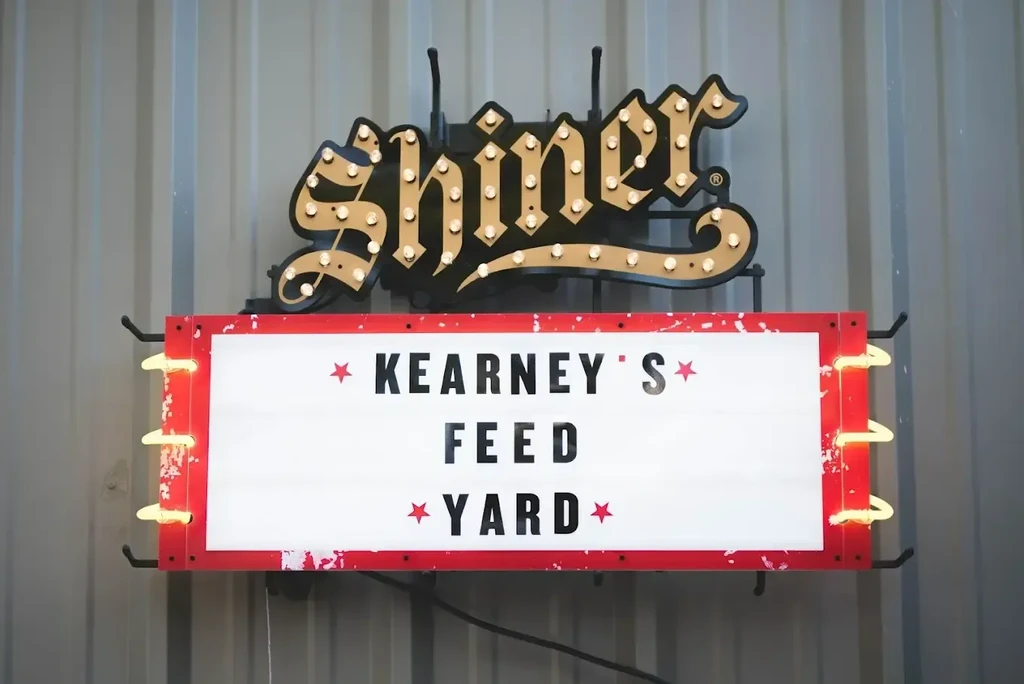 Vintage illuminated Shiner and Kearney's Feed Yard sign on metal wall.
