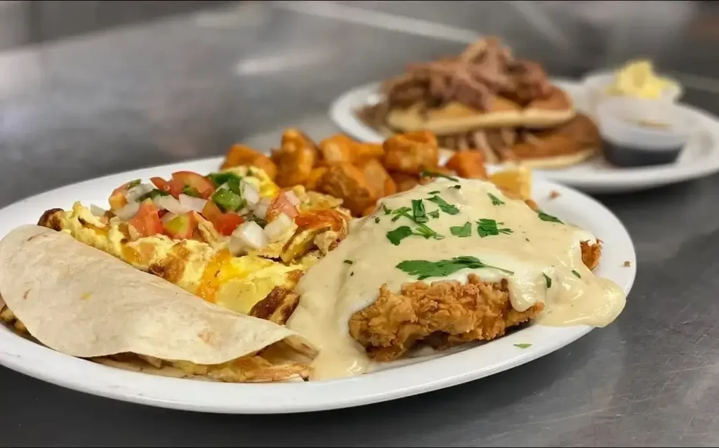 Multiple breakfast plates with fried chicken, eggs, and waffles.