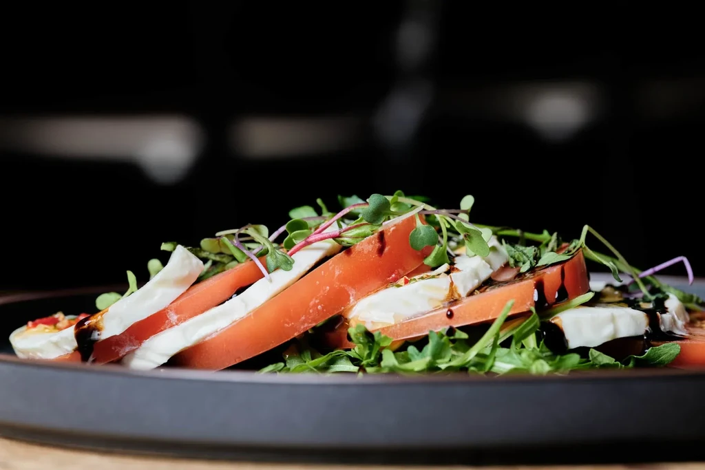 Plated Caprese salad with tomatoes, mozzarella, microgreens, and balsamic glaze.
