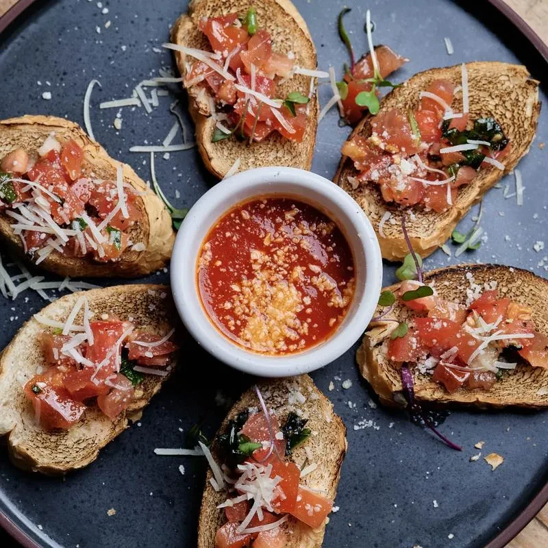 Six bruschetta pieces with tomatoes, herbs, cheese around red dipping sauce.