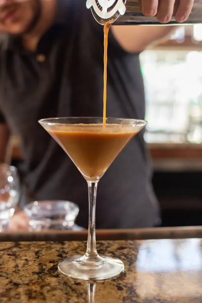 Amber cocktail being poured from a shaker into a martini glass.