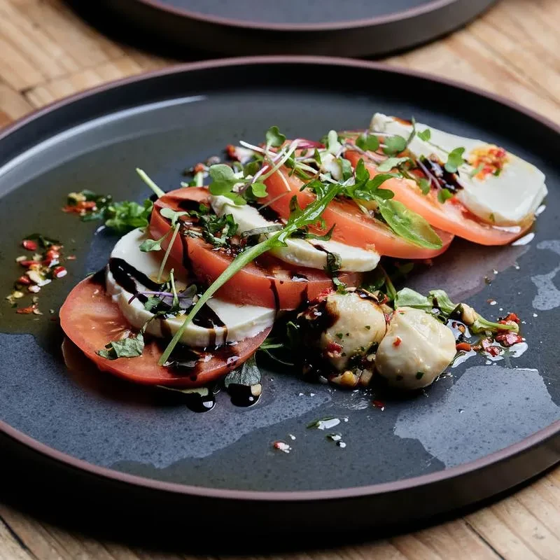 Beautifully plated Caprese salad with tomatoes, mozzarella, balsamic, and herbs.