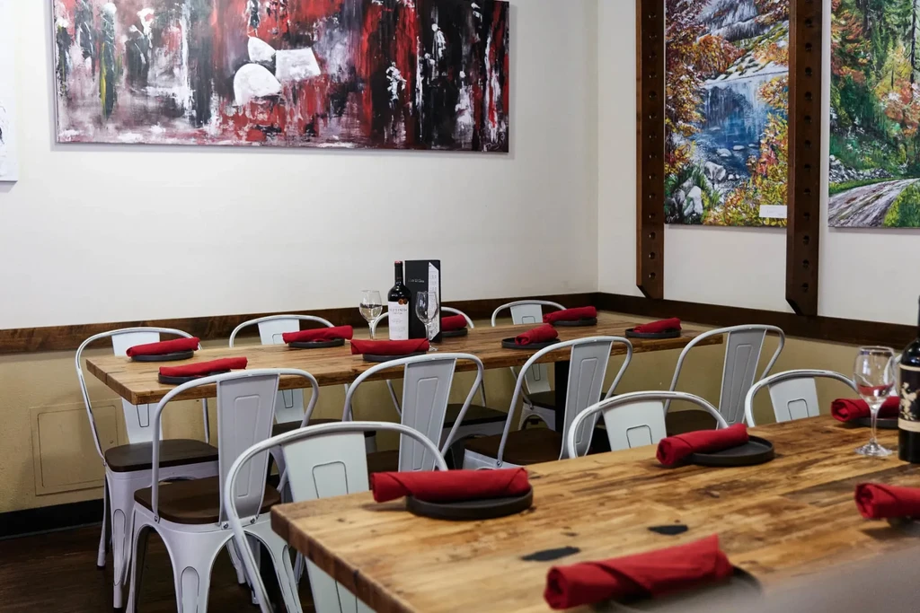 Empty restaurant dining room with a long table, wine, and wall art.
