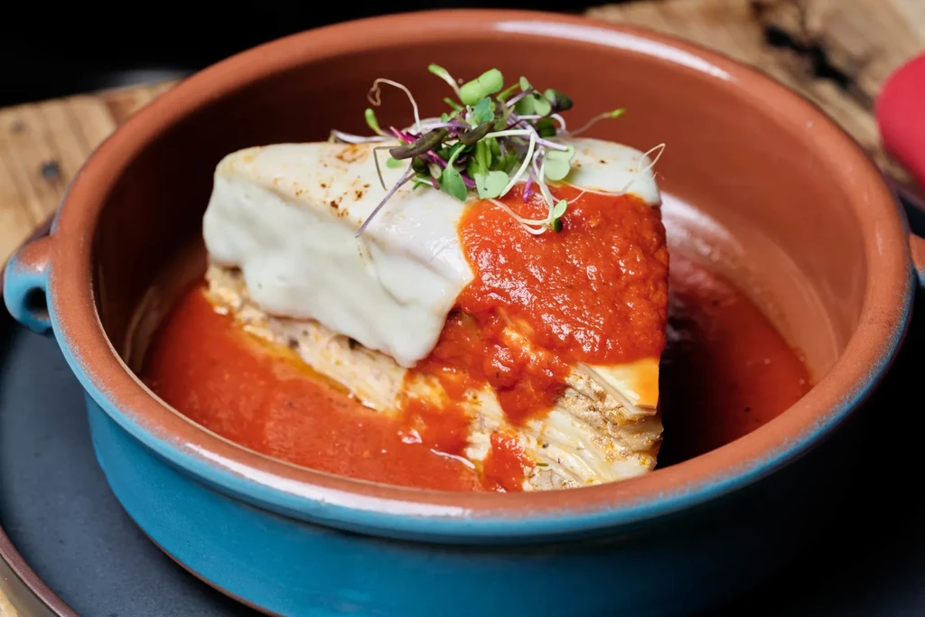 Layered dish with melted cheese, tomato sauce, and microgreens in a rustic bowl.