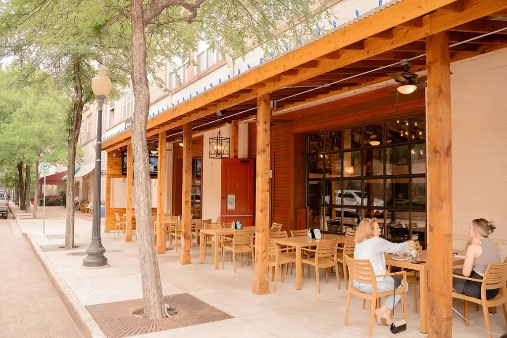 Restaurant patio with wooden pergola, metal roof, tables, and two women.