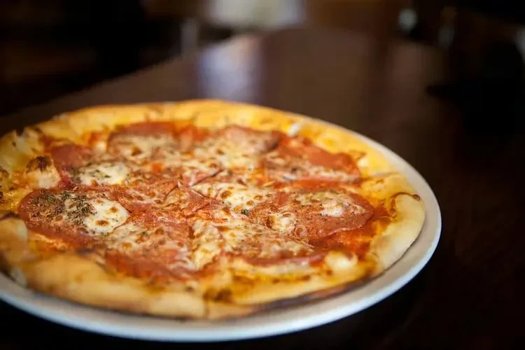 Freshly baked pepperoni pizza with melted cheese, herbs, cut on plate.