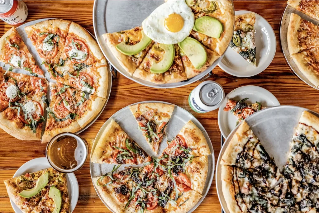 Overhead view of a table filled with various pizzas and drinks.