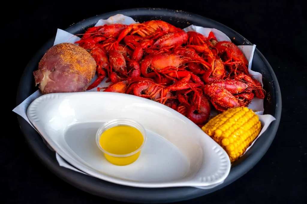 Cooked crawfish, seasoned potato, corn, and sauce on a dark platter.