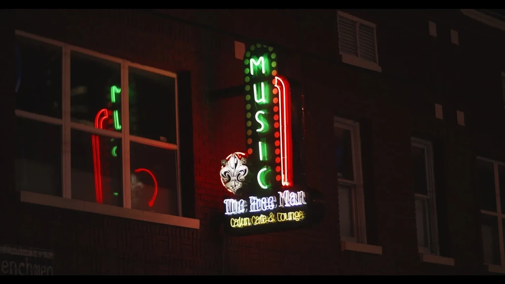 Vertical neon sign "MUSIC The Free Man Cajun Cafe" on brick building.