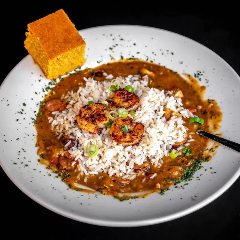 Professionally plated Cajun stew with shrimp, rice, cornbread, and green onions.
