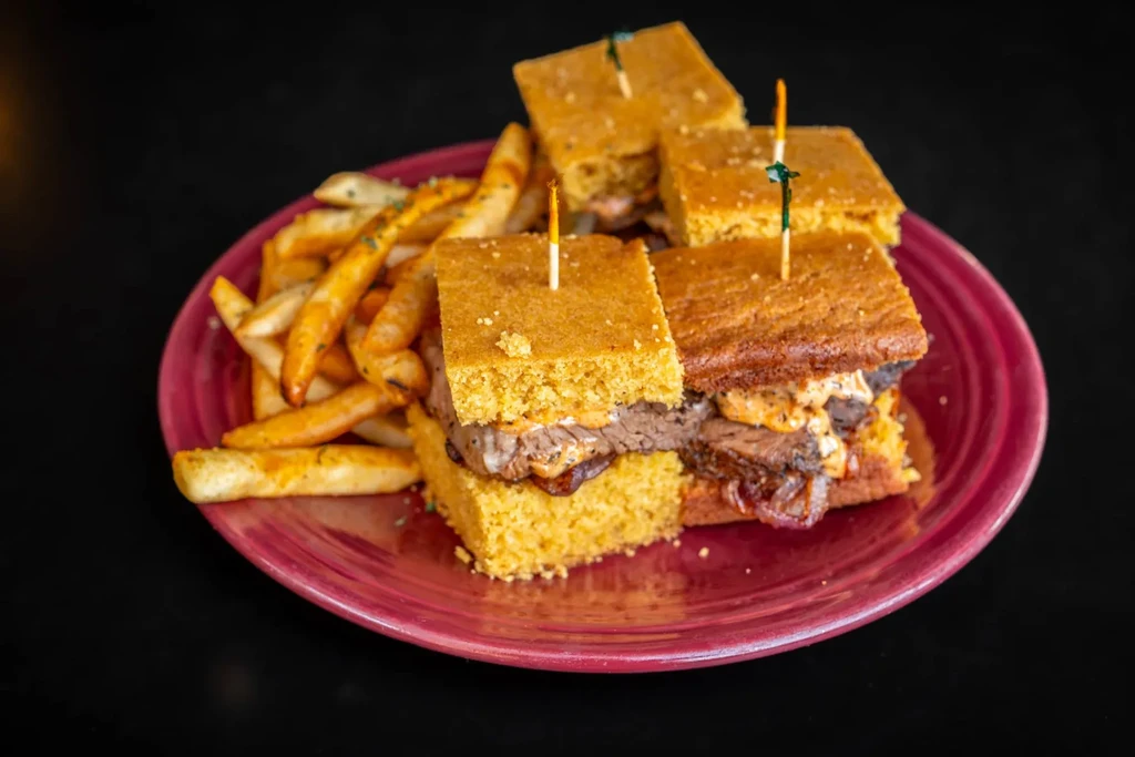 Four cornbread sliders with meat and herb fries on a red plate.