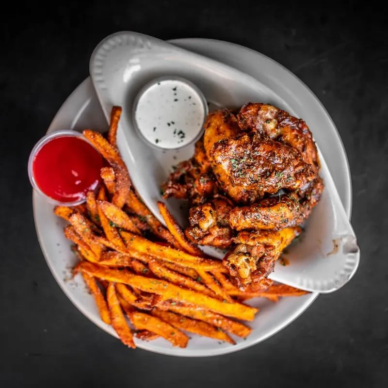 Crispy chicken wings in dark sauce, sweet potato fries, and two dips.