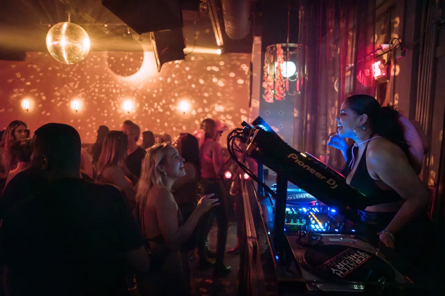 Woman DJ with cowboy hat performs for smiling club crowd.