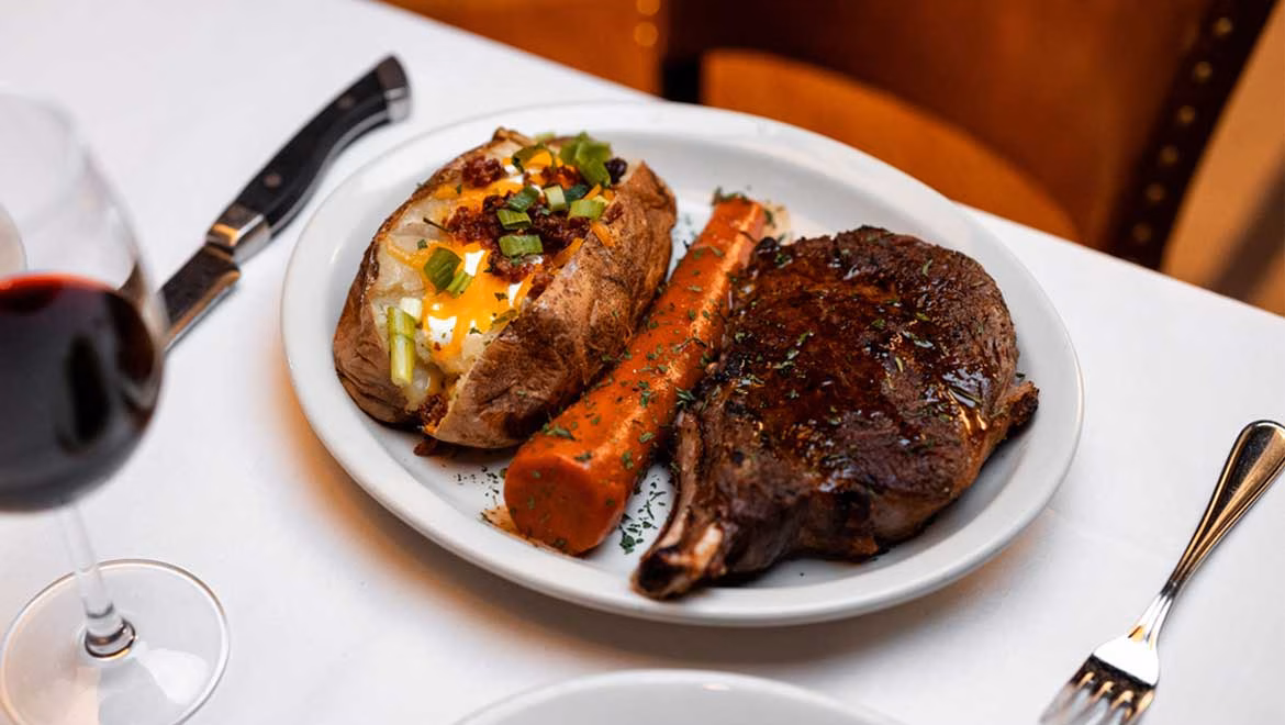 Steak, loaded baked potato, roasted carrot, and a glass of red wine.