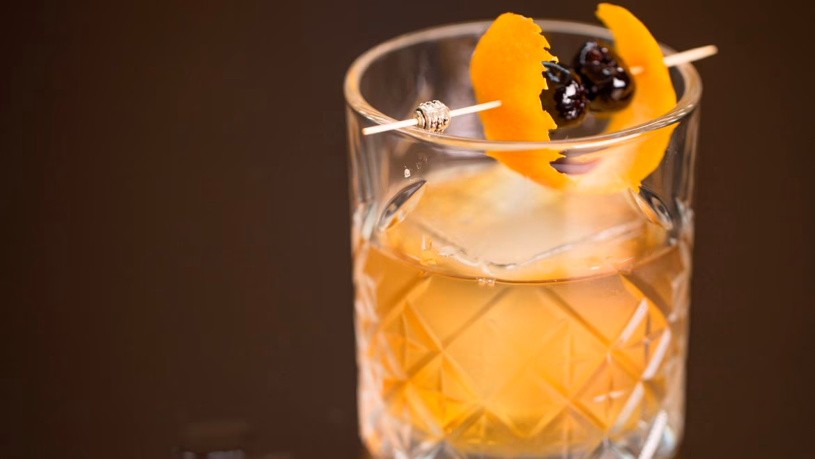 Cocktail in a patterned glass with ice, orange peel, and cherries.