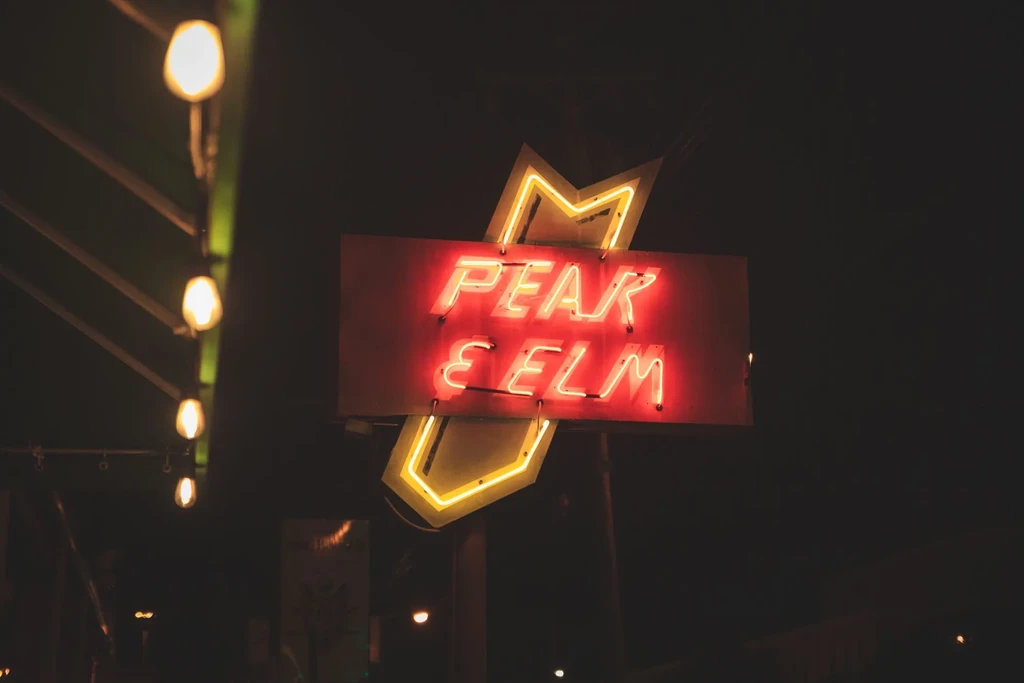 Red 'PEAK & ELM' neon sign with yellow star outline at night.