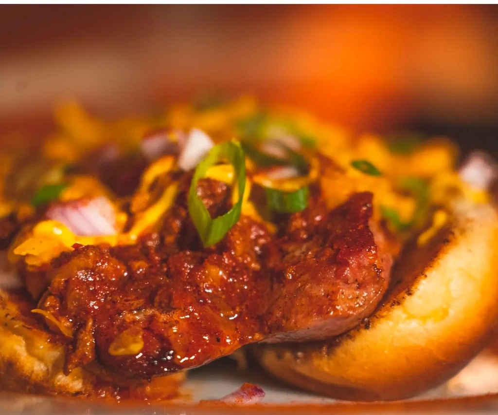 A chili dog, topped with melted cheese, red and green onions.