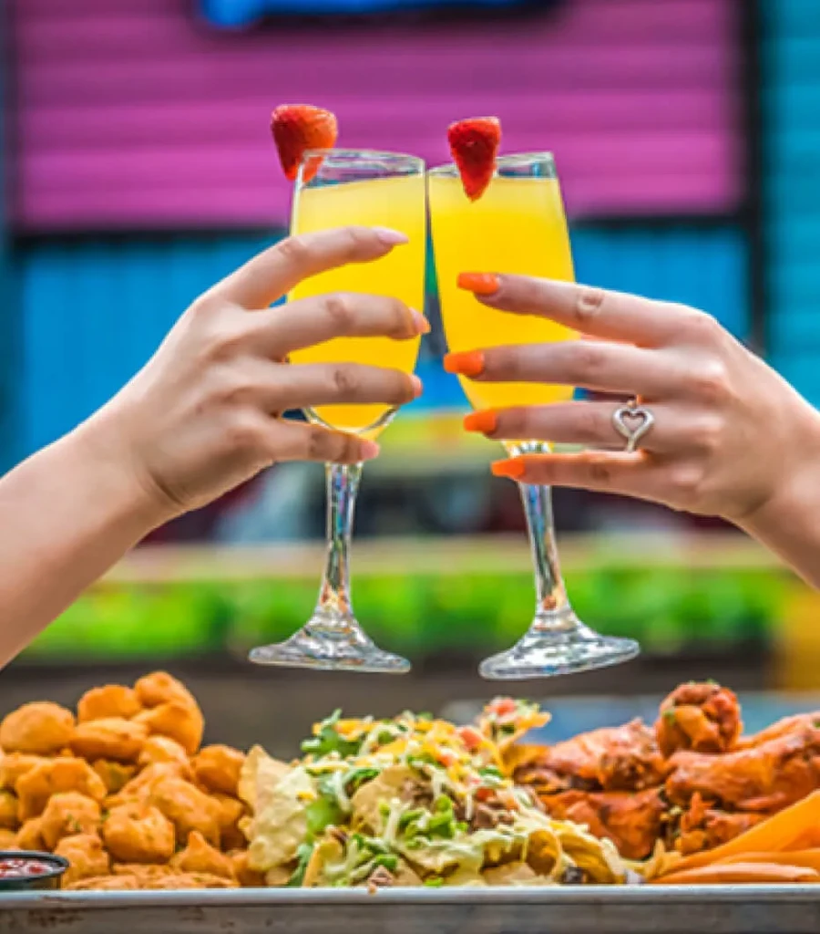 Hands toast mimosas over nachos, wings, and fried appetizers.