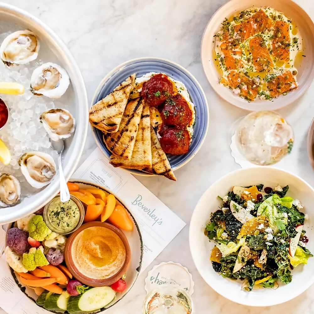 Overhead spread of oysters, meatballs, salmon, hummus crudites, salad